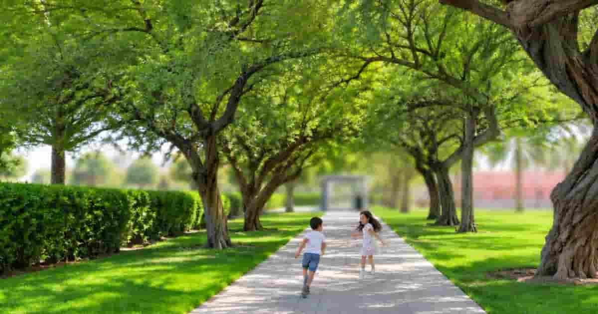 Park walkway with children playing under shady trees in Al Khor Family Park and zoo